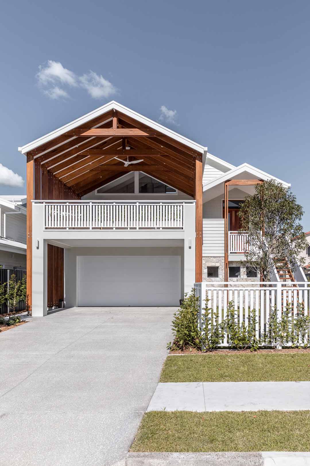 A bold queensland coastal home front façade with a large timber pavilion and white picket fence