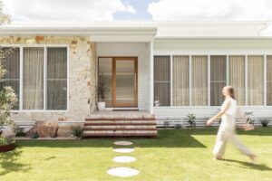 A modern house entry way with limestone crazy pave stone feature wall simple garden and a timber door with fluted glass