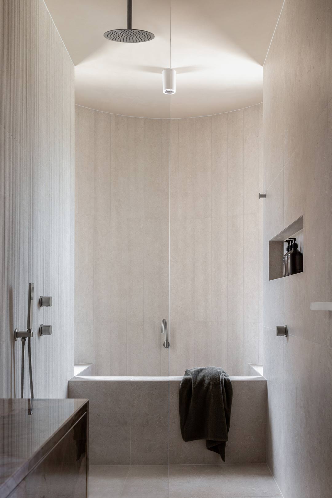 A spa like bathroom with a ceiling shower dropper and a built in concrete bath
