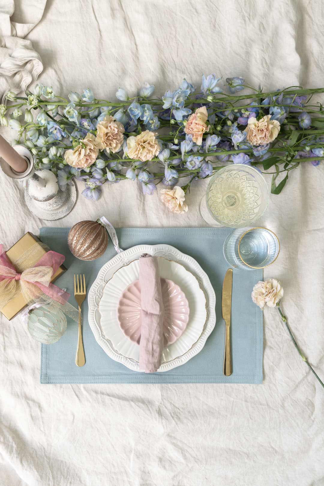 An elegant provincial style Christmas table setting with pastel colours like blue and pink with gold or brass accents and antique vintage charm