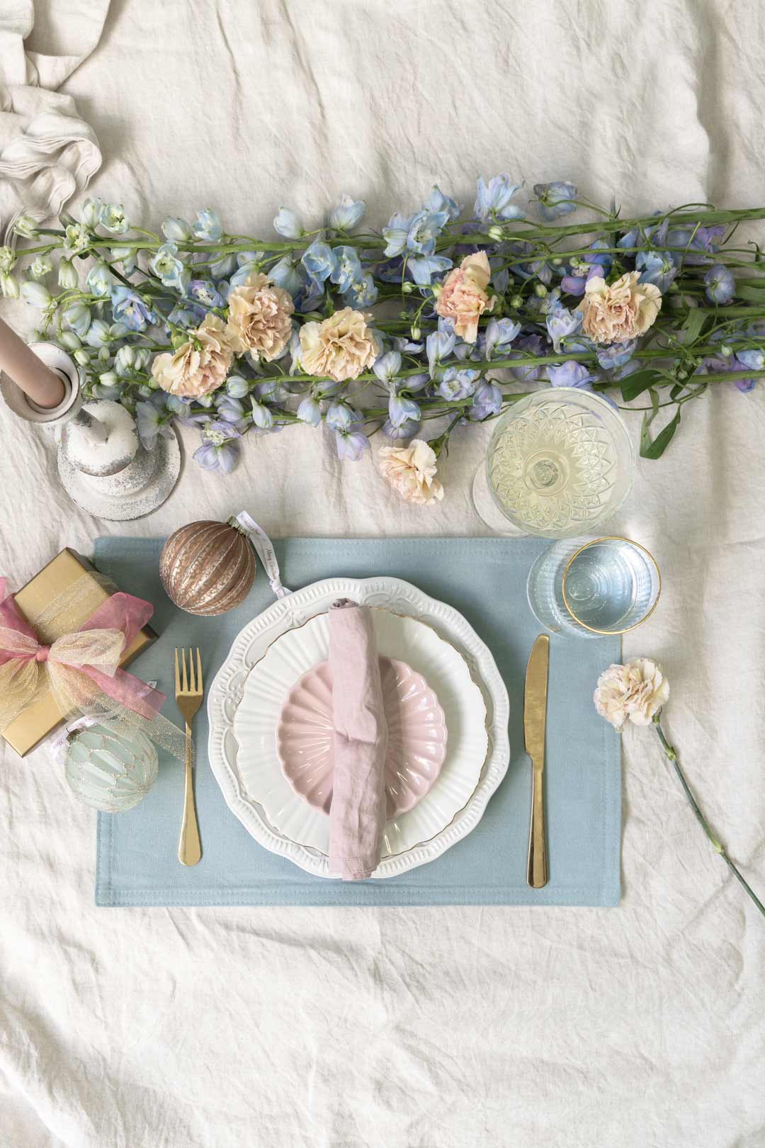 An elegant provincial style Christmas table setting with pastel colours like blue and pink with gold or brass accents and antique vintage charm