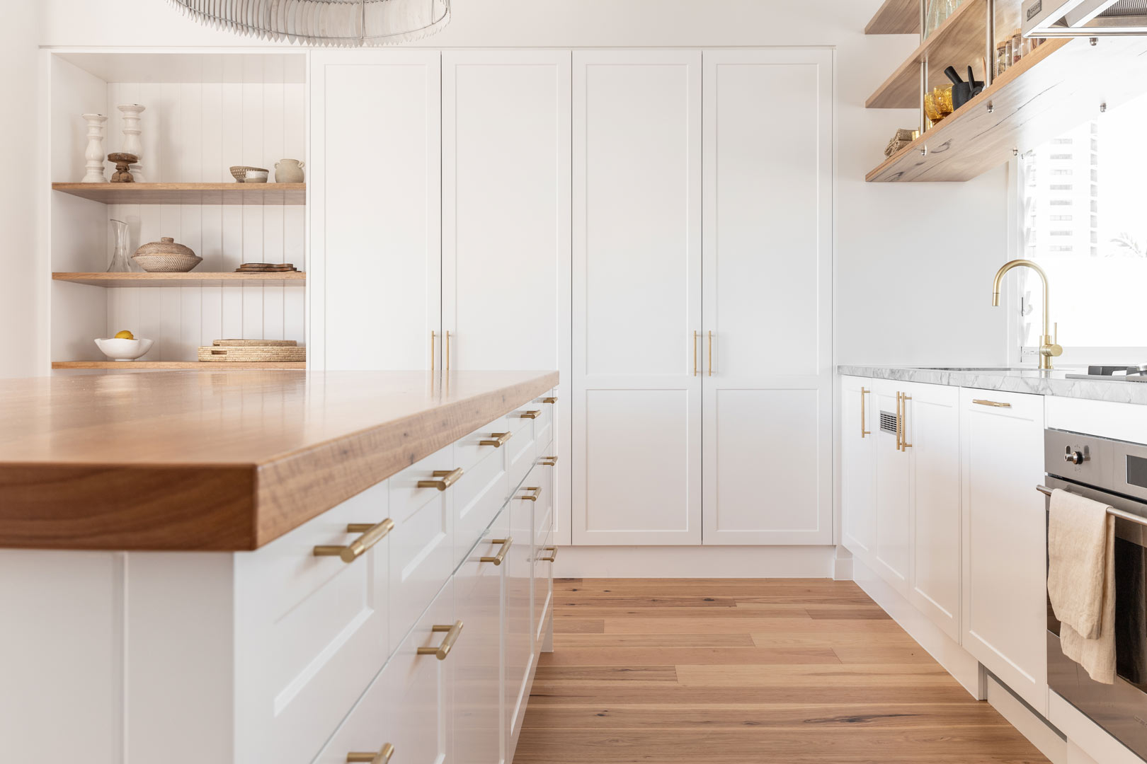 Coastal open plan living kitchen with white shaker cabinetry and brushed brass cabinetry pulls