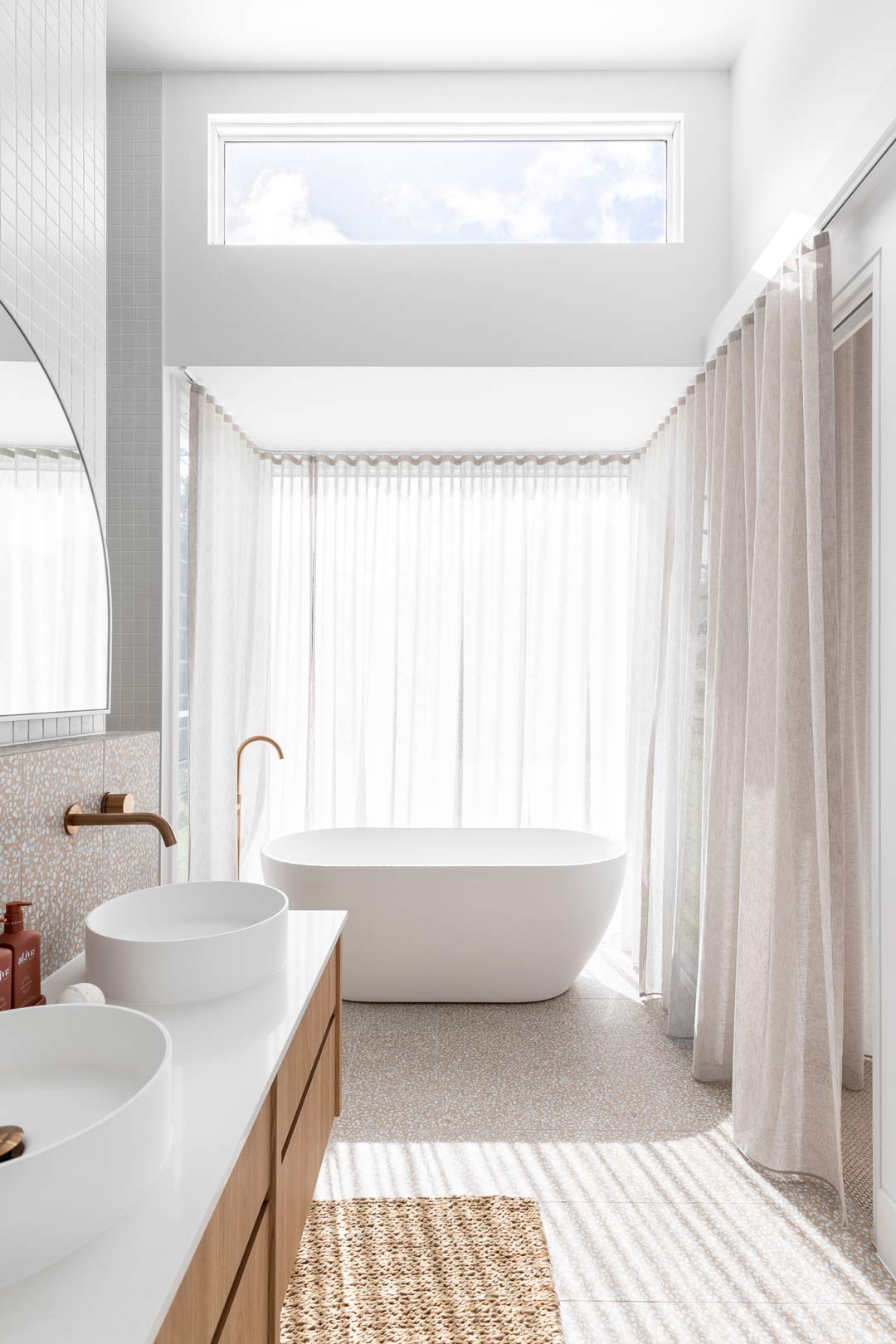Soft indirect daylighting brightening this bathroom through large windows with sheer curtains and clerestories